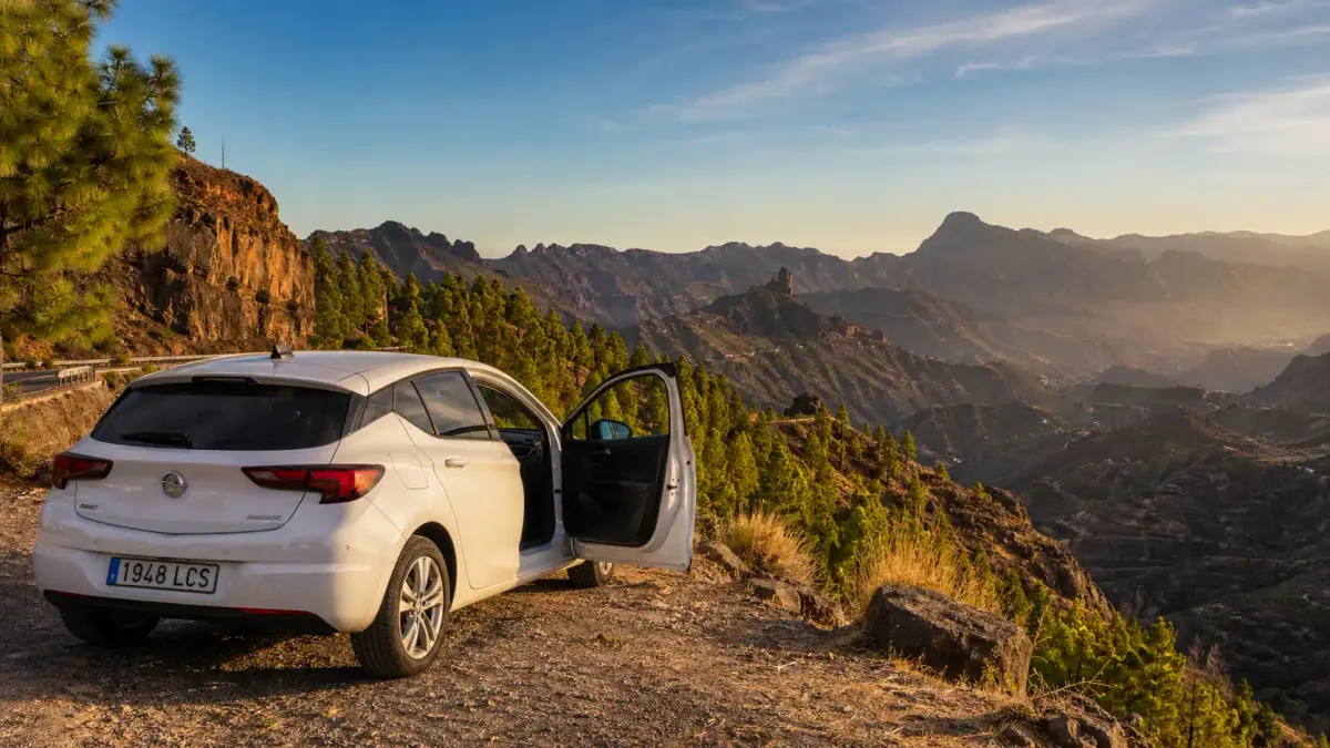 Auto a noleggio bianca parcheggiata su una strada di montagna a Gran Canaria, con pinete e picchi vulcanici sullo sfondo al tramonto